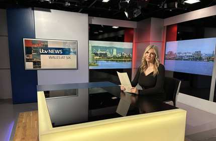 A person sat at a desk in a television news studio.