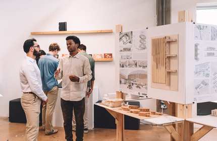 Two people stand beside a table featuring a display of architectural models, engaged in conversation.