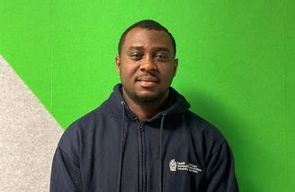 A man in a blue sweatshirt poses against a bright green wall, creating a striking visual contrast.