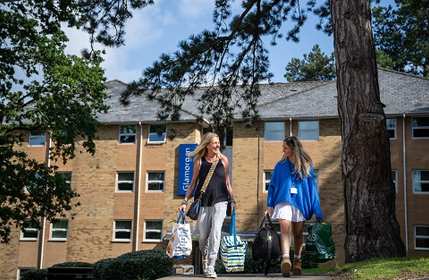 Student and parent carry bags through the Plas Gwyn campus green areas