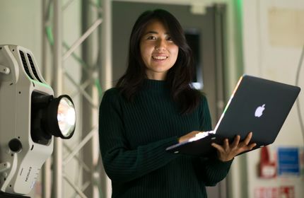 A Woman in a dark green jumper stands holding an open laptop