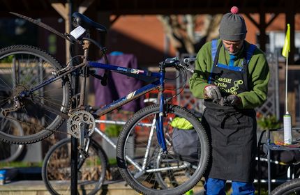 A man inspects a metal bolt in his hands while repairing a bicycle raised on a stand