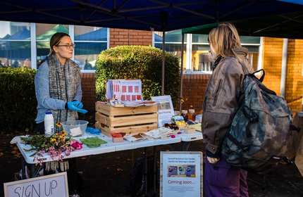 A young woman stands at a Sustainability information stand during a Community Event on Llandaff Campus