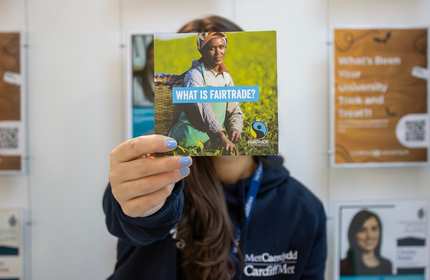 Cardiff Met staff member holds a fairtrade information leaflet in front of their face