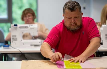 A man sorts through colourful papers at a desk in a busy classroom