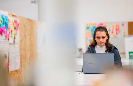 A young adult works from a laptop in an arts workspace