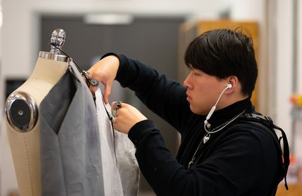 A young adult adjusts a piece of fabric dressed on a mannequin