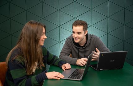 Two young adults have a conversation while working from their laptops