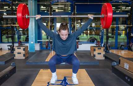 A woman executing a squat in a gym setting, highlighting her commitment to strength training and healthy living.