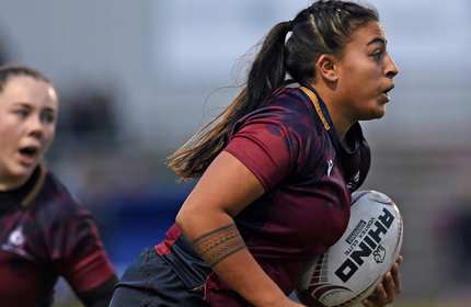 Two women in maroon jerseys engaged in a rugby match, showcasing teamwork and athleticism on the field.