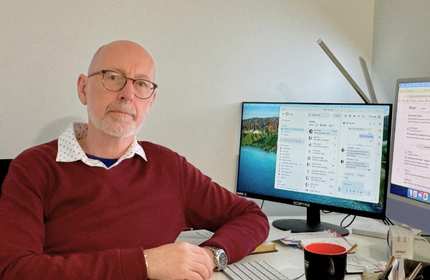 A bald man works at a desk with two computer monitors, engaged in tasks in a professional environment.