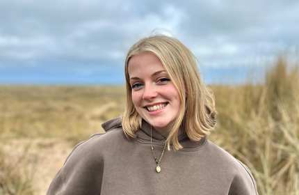 A woman wearing a brown hoodie smiles warmly at the camera.