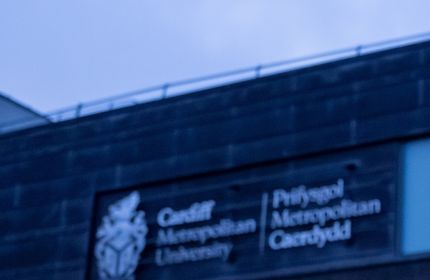 Kush Shinde, in graduate cap and gown, holds a purple Cardiff Met sign with both hands