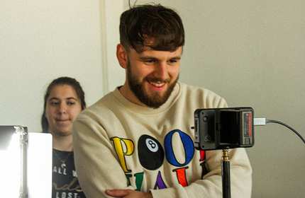 Man in a cream graphic sweatshirt looks into a digital camera set on a stand