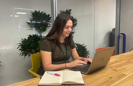 Zoe Moore works on a laptop while sat at a wooden desk