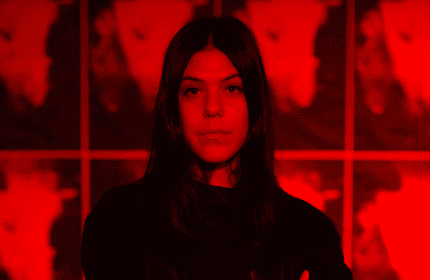 A woman in black attire poses against a striking red light backdrop.