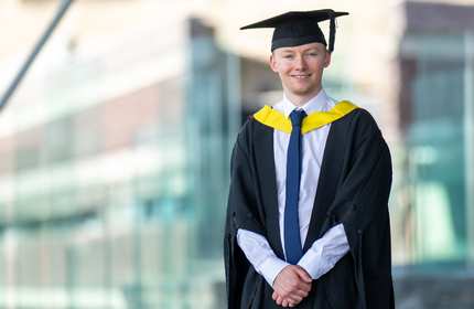 A man wearing a graduation gown and cap, celebrating his academic achievement with a proud smile.