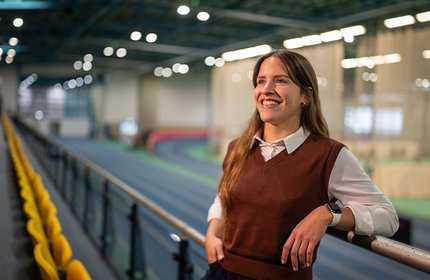 A woman stands confidently in front of an indoor race track.