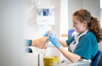 A woman wearing a blue shirt and gloves is having her foot examined by a healthcare professional.
