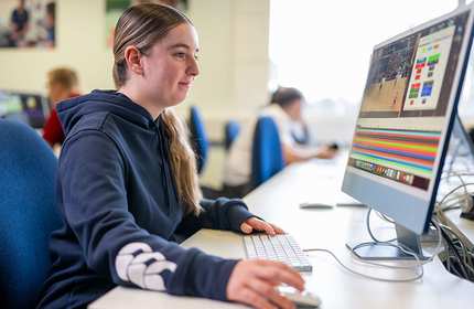 A young woman in a navy blue hoodie uses a keyboard and mouse while looking at a computer screen