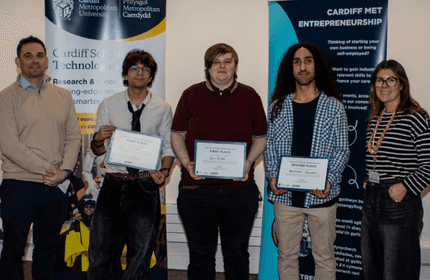 Three Cardiff Met students hold certificates of award, with a lecturer either side of them