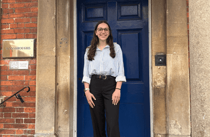 A young woman in a stripe shirt and black trousers poses for a photograph in front of a building entrance