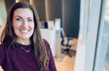 A woman takes a selfie beside a bright window in a large office space