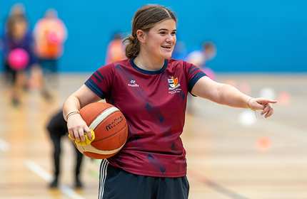 Sport Coaching student holds a basketball under one arm and points with the other to give instruction