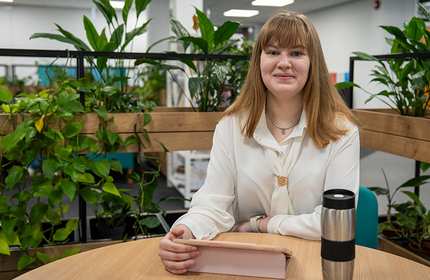 A young woman sits at a round table working on a tablet, surrounded by plants