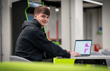 A young man works on a laptop at a table in an open workspace