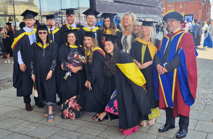 A group of graduating students, in graduation gowns and caps, pose for a photograph