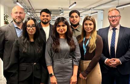 A group of smartly dressed individuals stand for a photograph in an office