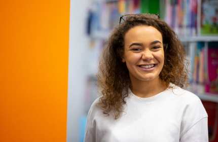 A young woman stands beside an orange wall