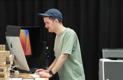 A man wearing a hat is focused on working at his computer.