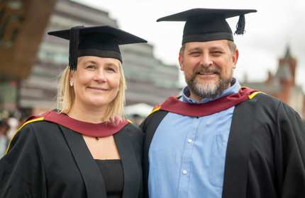 A man and woman in graduation caps and gowns stand side by side.