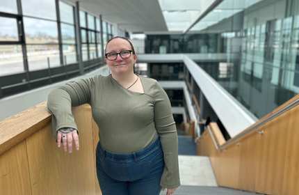 A young woman stands on a staircase in a bright, atrium space.