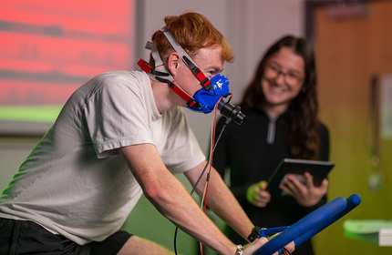 A person on an exercise bike wearing an oxygen mask.