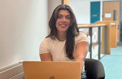 A person wearing a t-shirt sits in front of an open laptop computer.