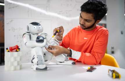 A person makes an adjustment to a small humanoid robot.