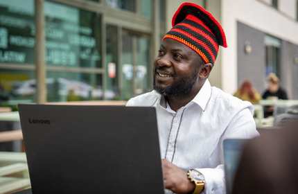 A man wearing a white shirt uses a laptop in an outdoor seating area.