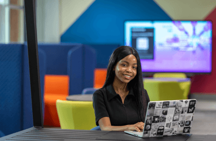 A woman seated at a table, focused on her laptop, engaged in work or study.