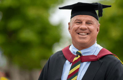 A smiling man wearing a graduation gown, celebrating his academic achievement.