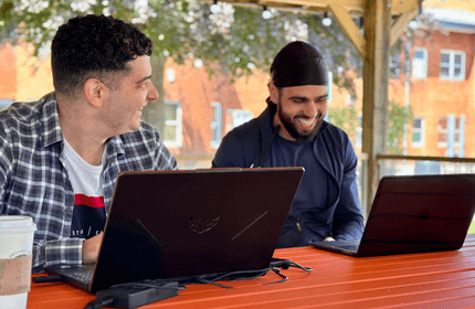 Two Cardiff Met students talking while working from their laptops