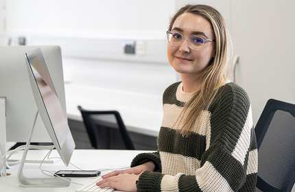 Woman wearing a striped jumper and glasses sits at a computer desk