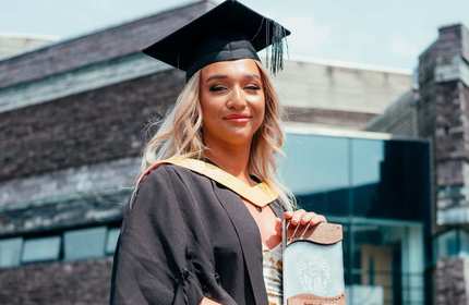 Amber Cripps, in graduation cap and gown, holds a wood and glass award