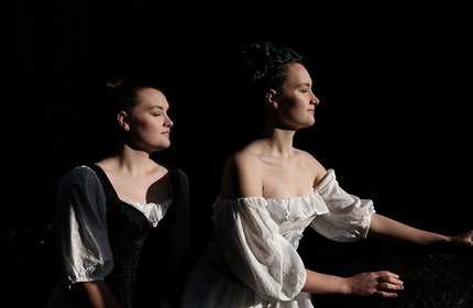 Two women wearing dresses stand together during a photoshoot