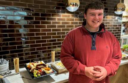 Charlie Lewis holds a small drinking glass and stands in front of a buffet table