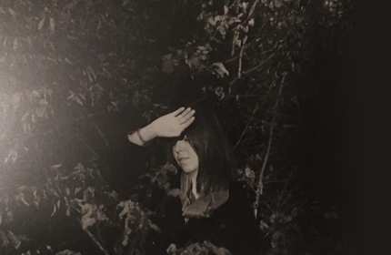 A black and white photograph of Ekaterina Kormilitsyna holding the back of her hand above her head to shade her eyes from the sunlight