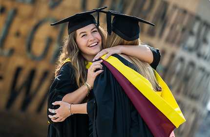 Two students, wearing graduate caps and gowns, embrace outside the Wales Millennium Centre