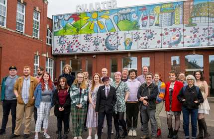 A large group of individuals stands outside the Chapter Arts Centre, below a large colourful mural